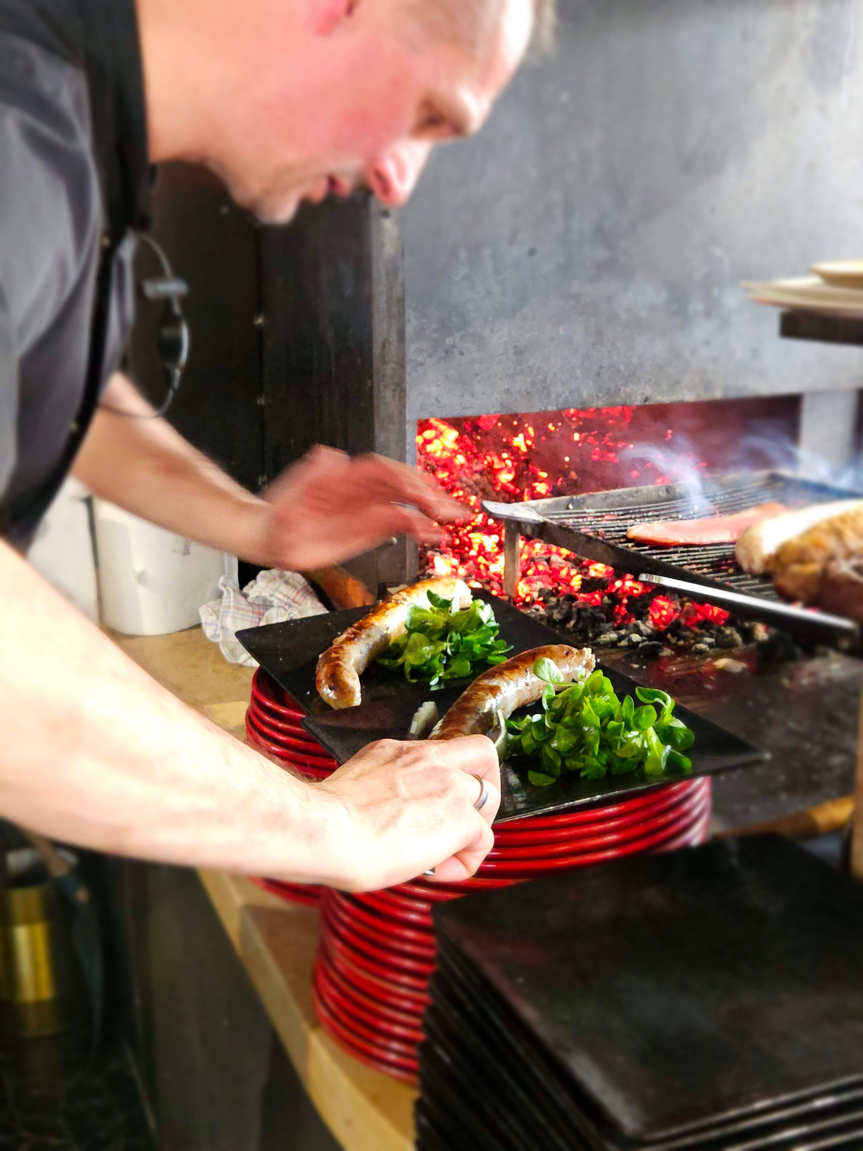 Chef en pleine cuisson de viandes au feu de bois dans la cuisine du restaurant Table 23 à Carquefou